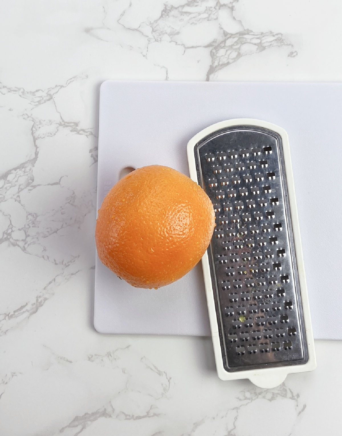 Orange on a white cutting board with a food grater. 