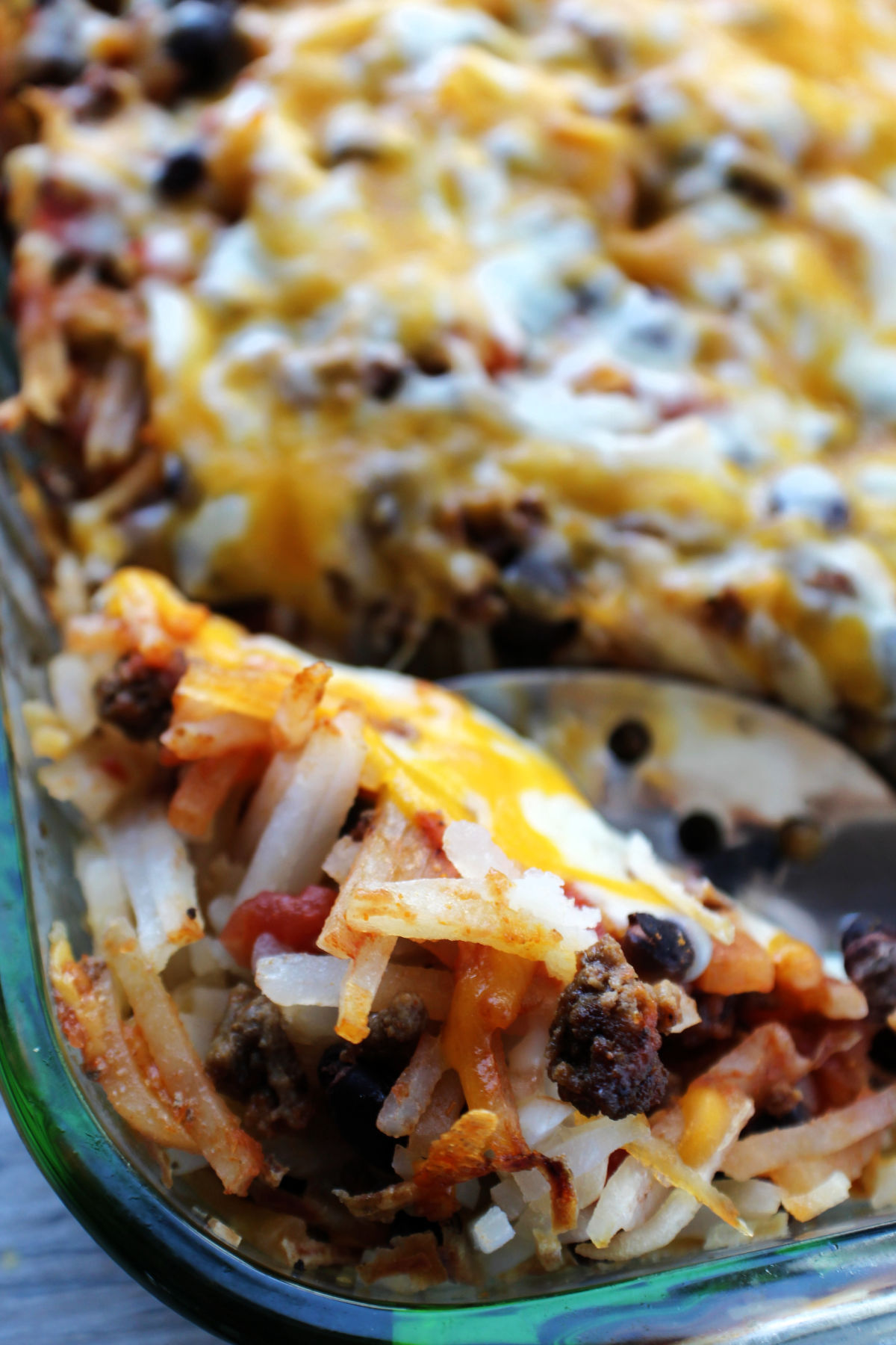 Hashbrown casserole with beans, hamburger and cheese in a casserole dish. 