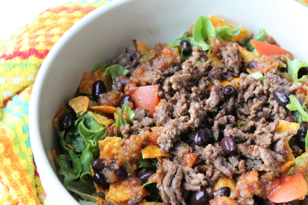 hamburger and lettuce, tomatoes and Doritos in a white bowl.  