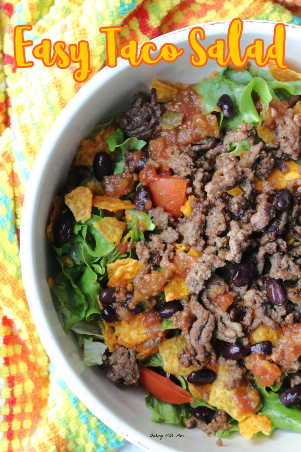 Taco salad with hamburger, tomatoes, beans and lettuce in a white bowl. 