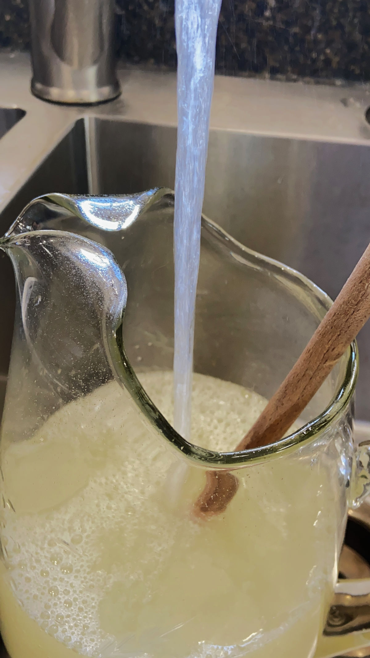 Lemonade in a pitcher at a sink with water being poured in. 