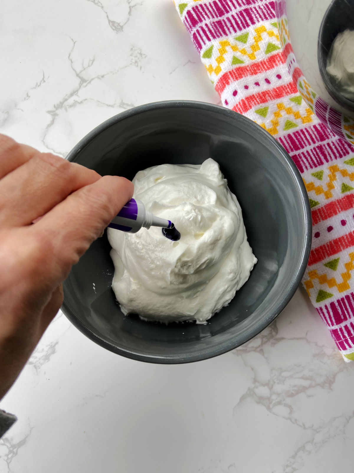 Purple food coloring being added in to a bowl of whipping cream. 