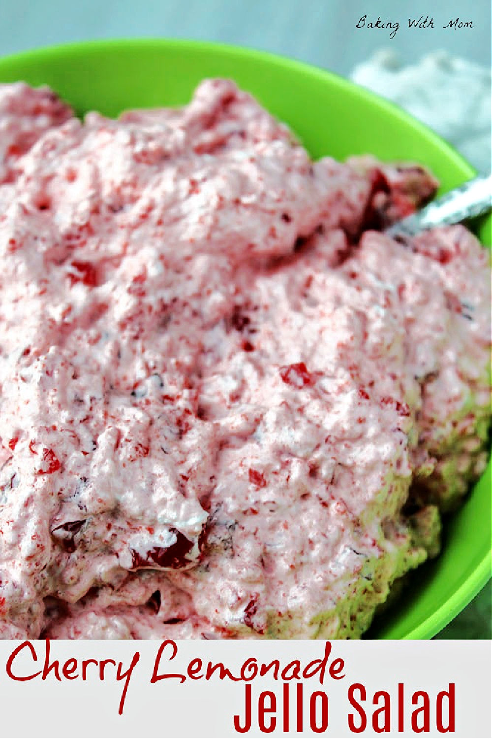 Cherry Jell-O salad in a green bowl with a serving spoon. 