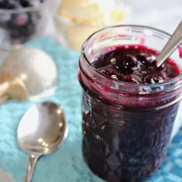 Blueberry sauce in a clear jar with a spoon nearby.