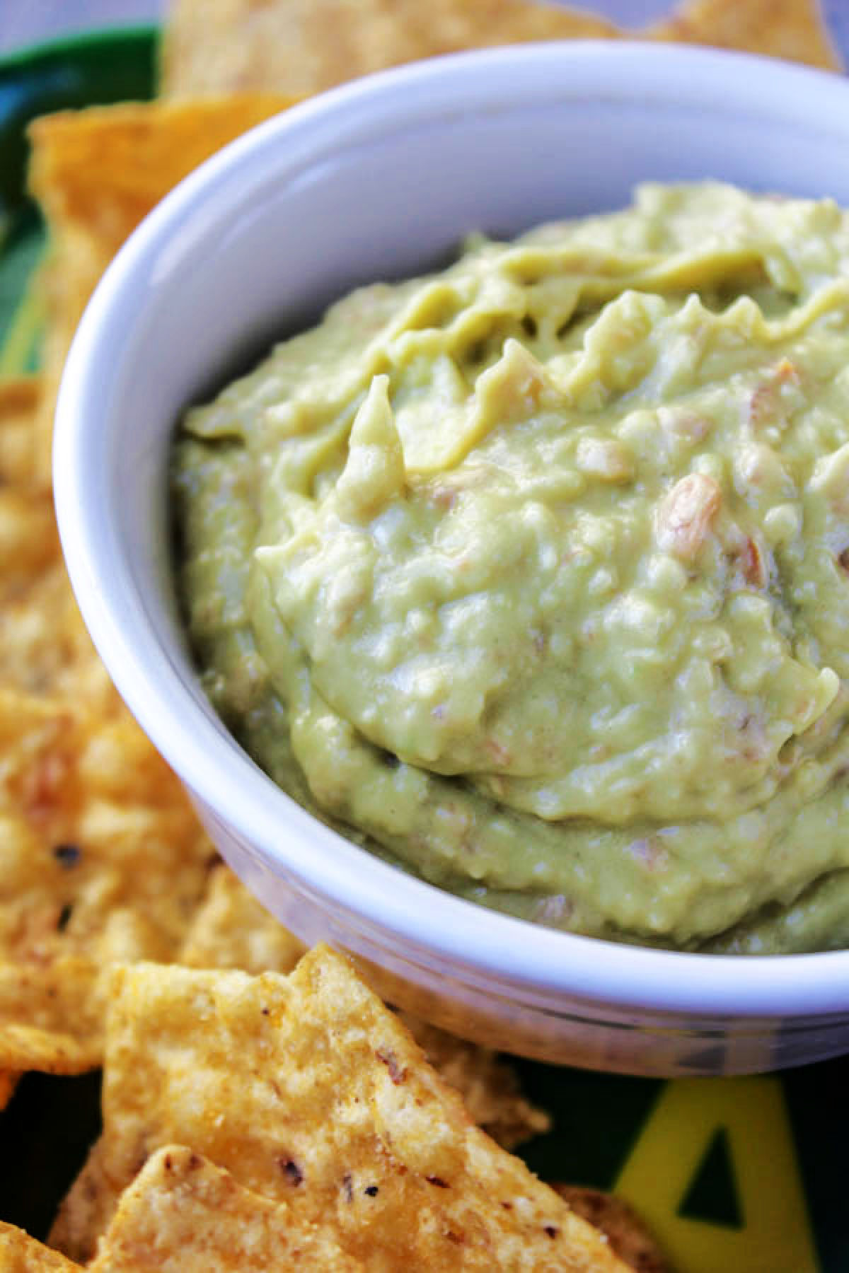 Bowl of guacamole dip in a white bowl with chips besides. 