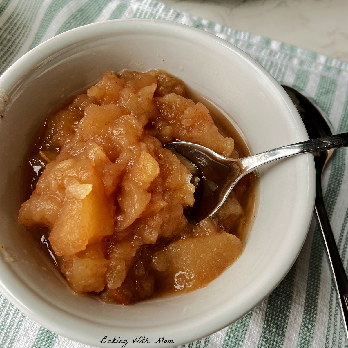 homemade applesauce in a white bowl with a crock pot behind.