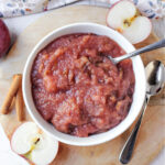 crock pot applesauce in a white bowl with apples besides.