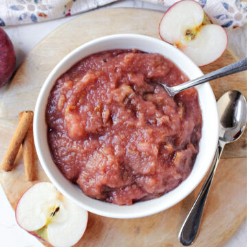 crock pot applesauce in a white bowl with apples besides.