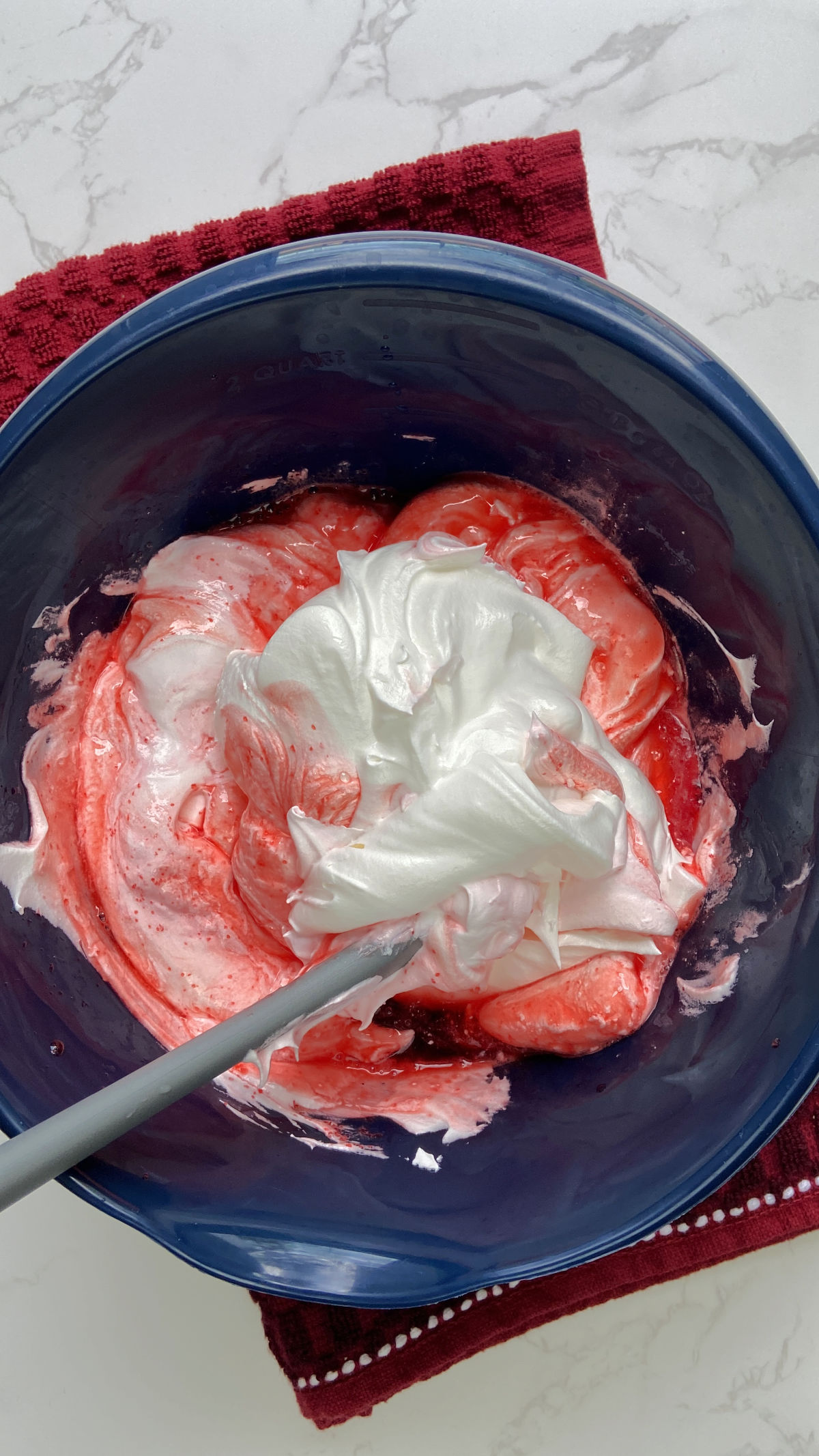 Folding whipped cream into the Jell-O mixture in a blue bowl. 