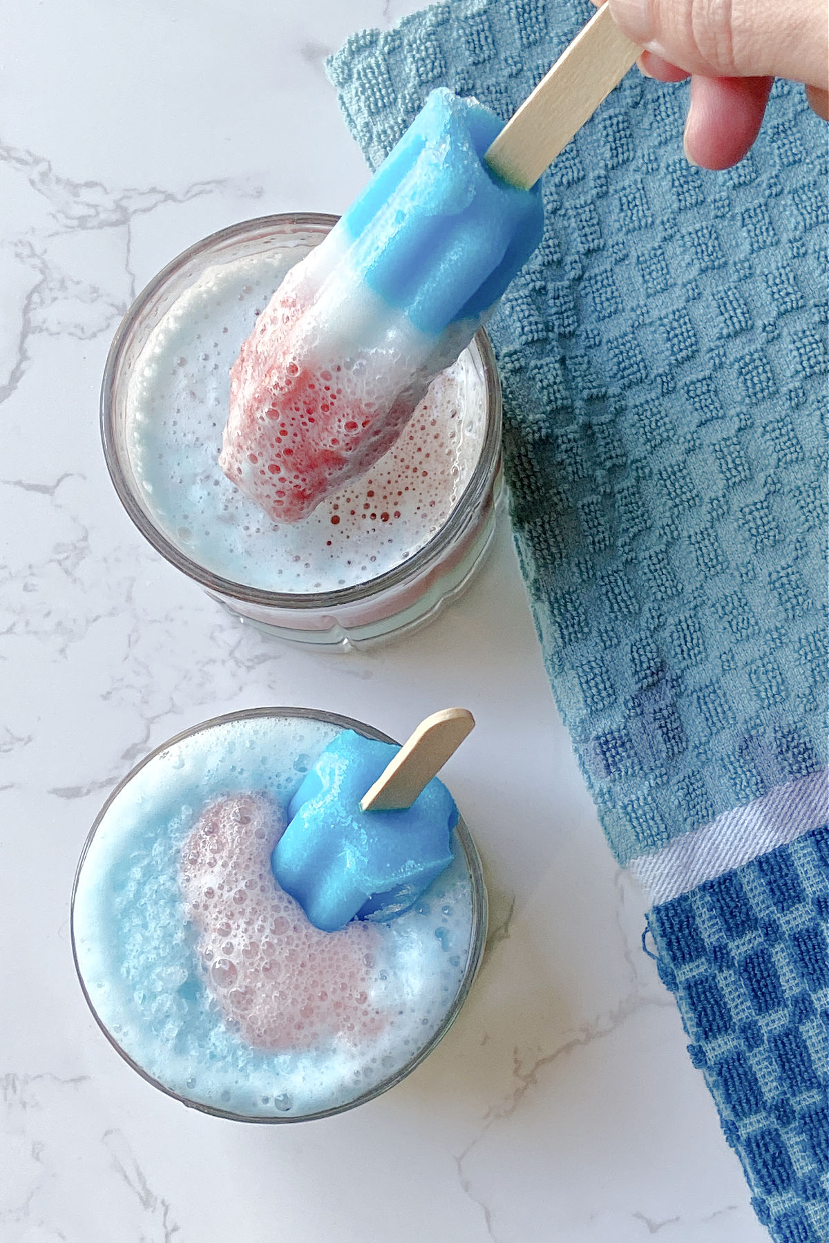 Two glasses with blue drink inside and Bomb Pop inside with a blue towel. 