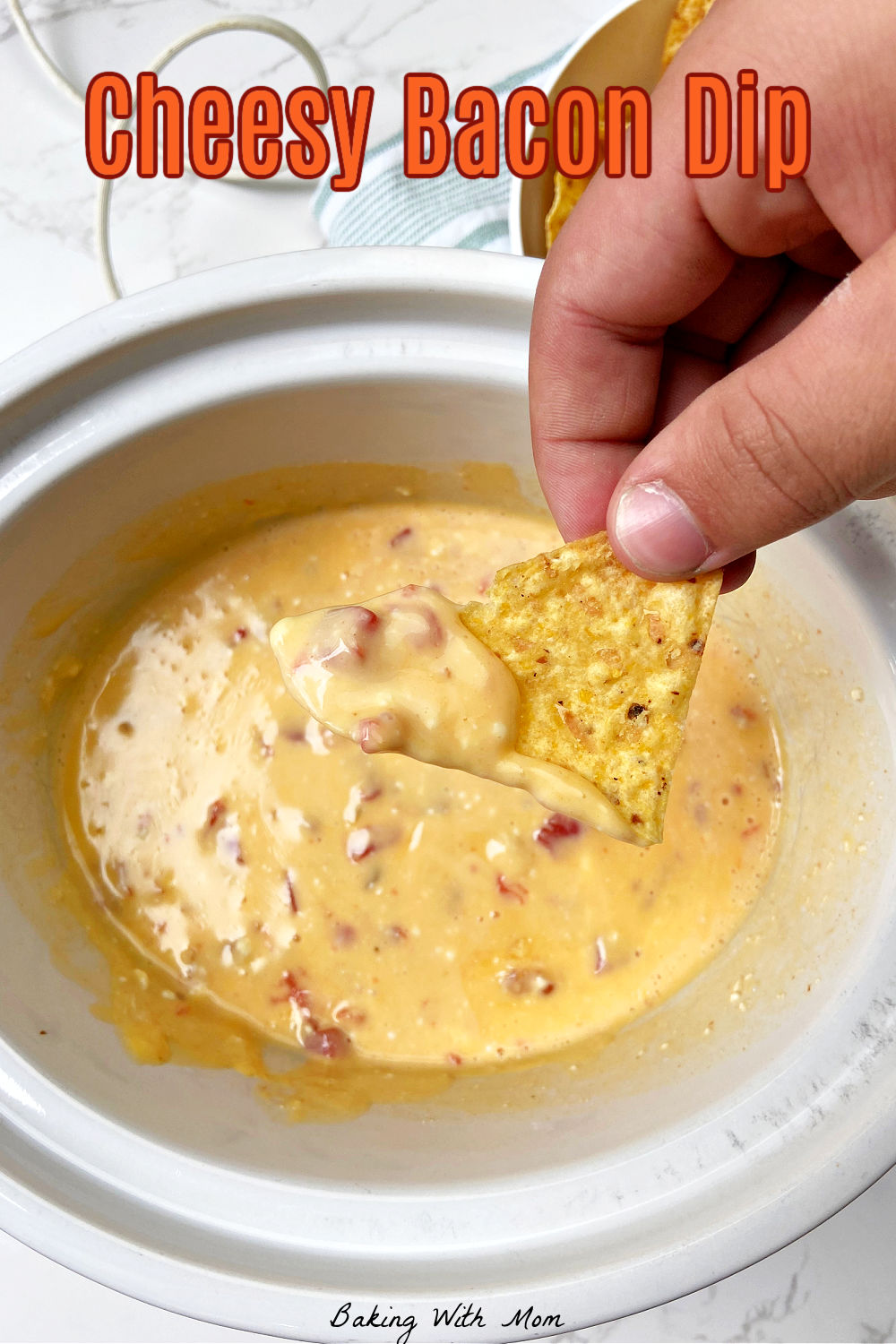 Melted cheese in a white crock pot with a hand holding a chip. 