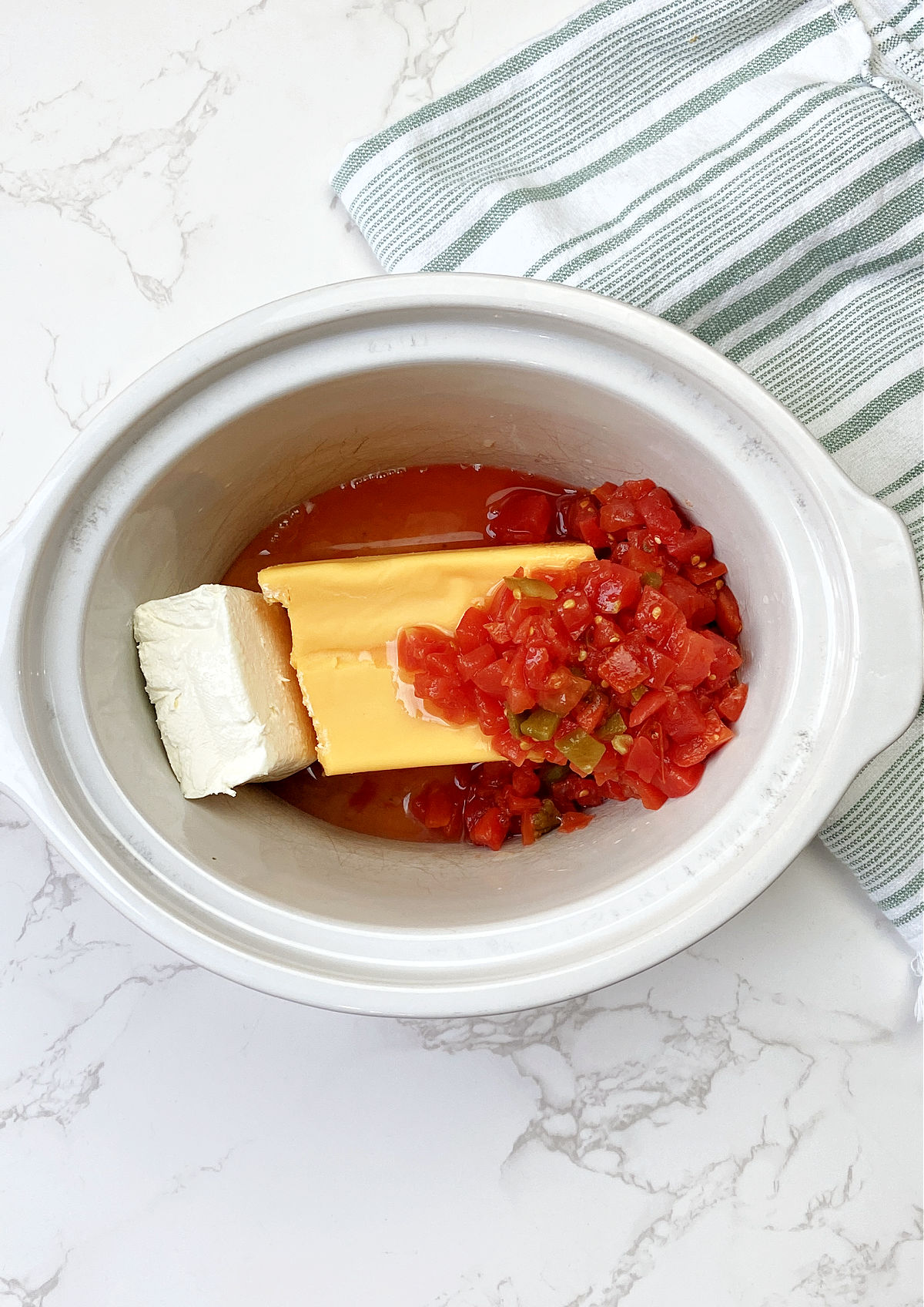 Cheese, tomatoes and cream cheese in a white crock pot. 