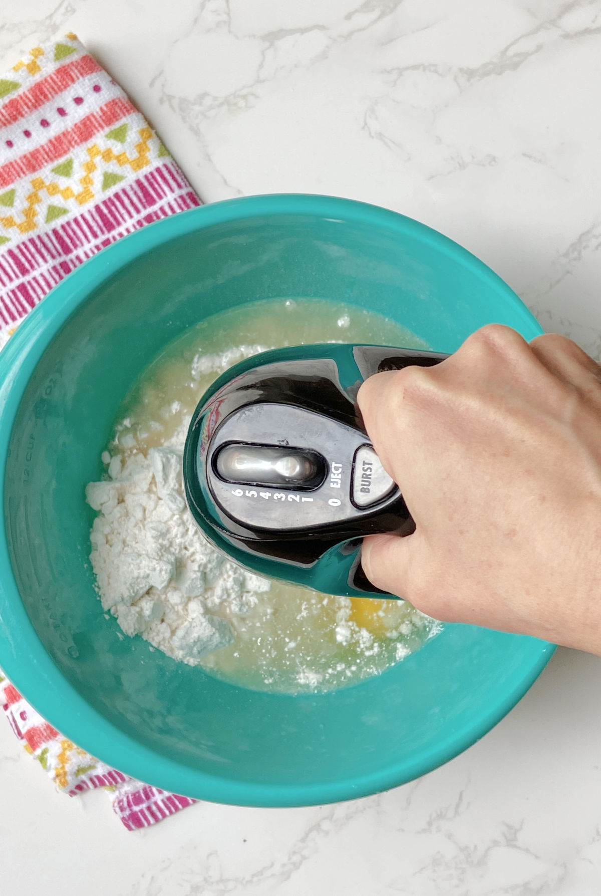 Hand mixer in a blue bowl mixing cake mix. 