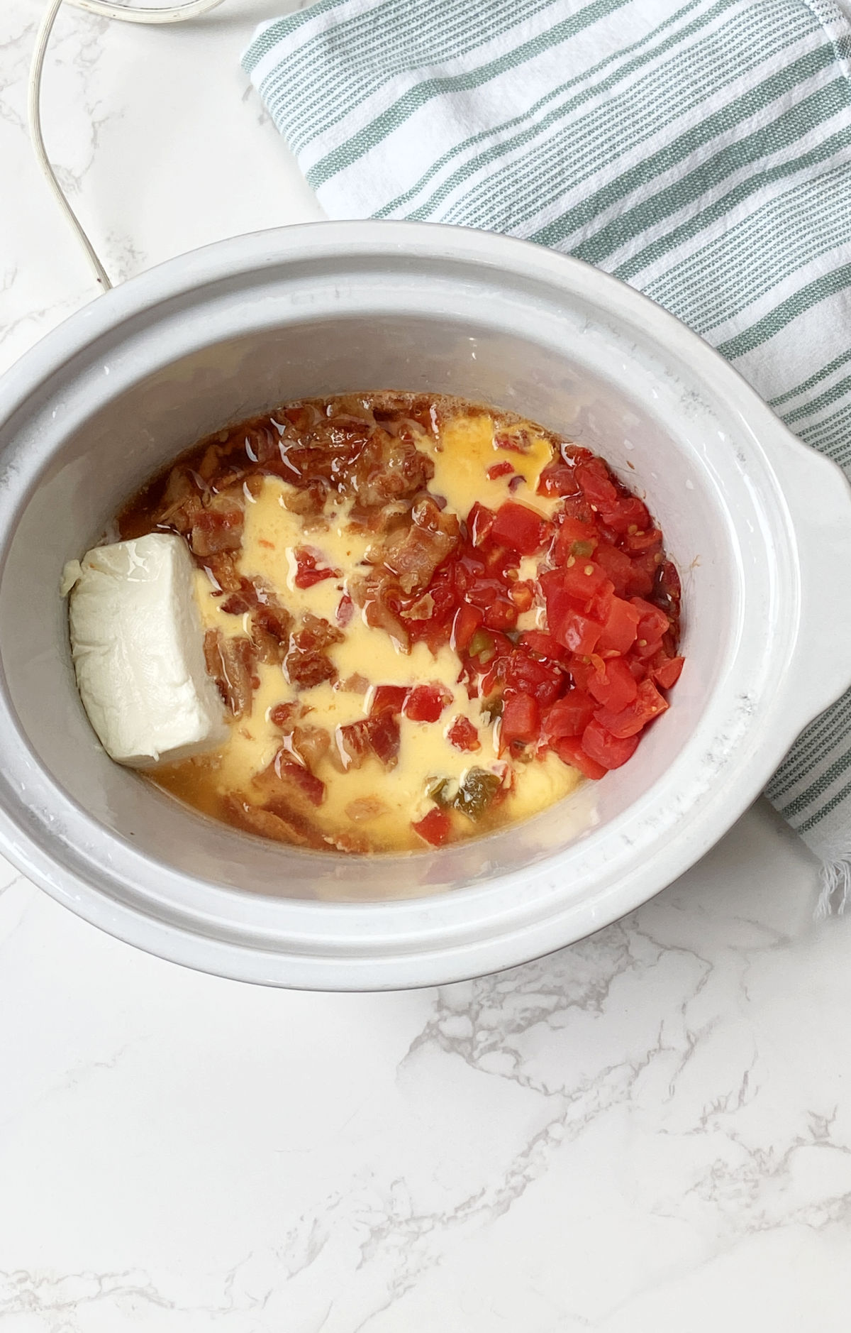 Melted cheese, cream cheese and tomatoes and bacon in a white crockpot. 