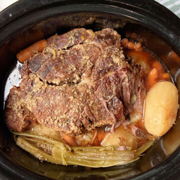 pot roast in a crock pot with potatoes and carrots.