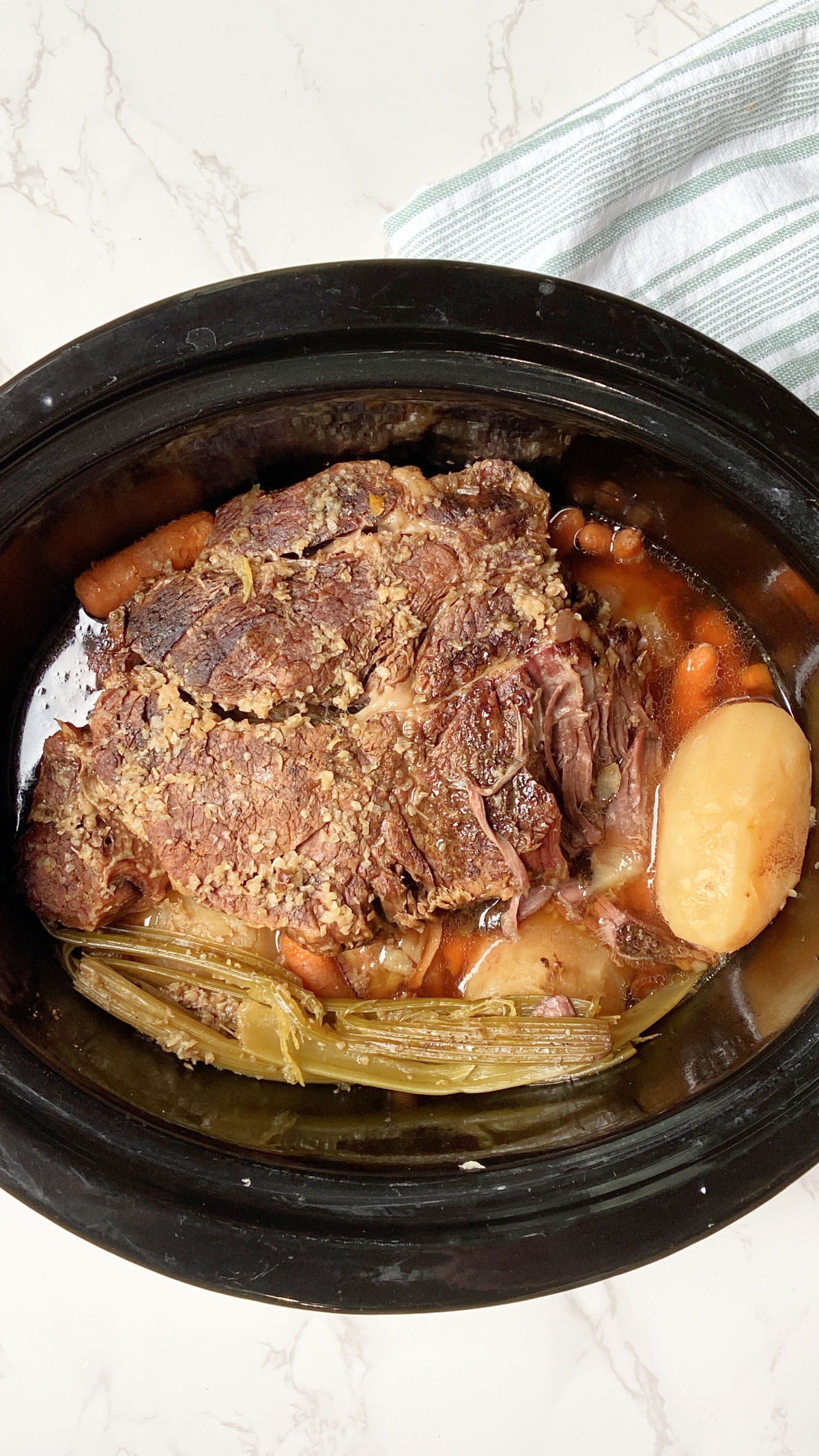 pot roast and potatoes in a crock pot with a towel laying besides. 