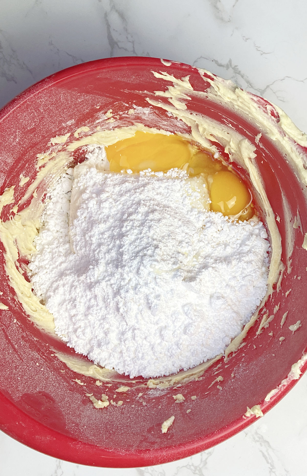 powdered sugar, eggs and cream cheese in a red mixing bowl. 