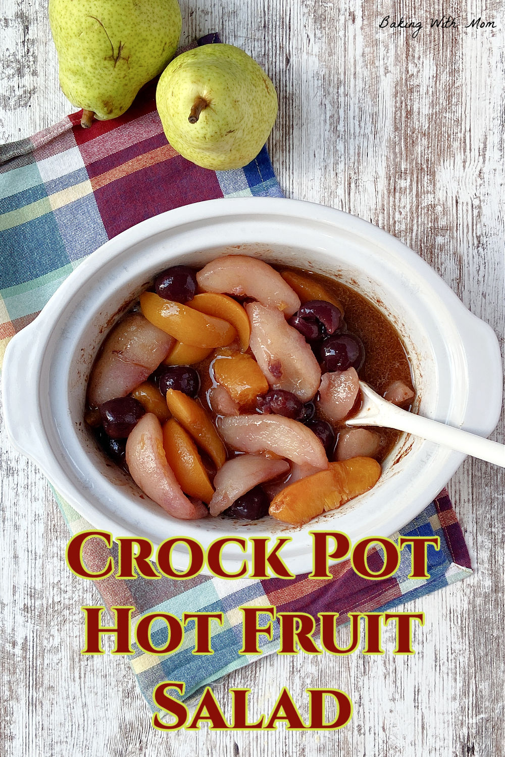 Fruit salad in a crock pot with a checkered red and blue towel underneath. 