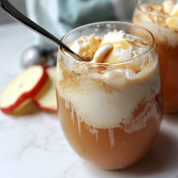 apple cider in a clear glass with a scoop of vanilla ice cream and caramel on top.