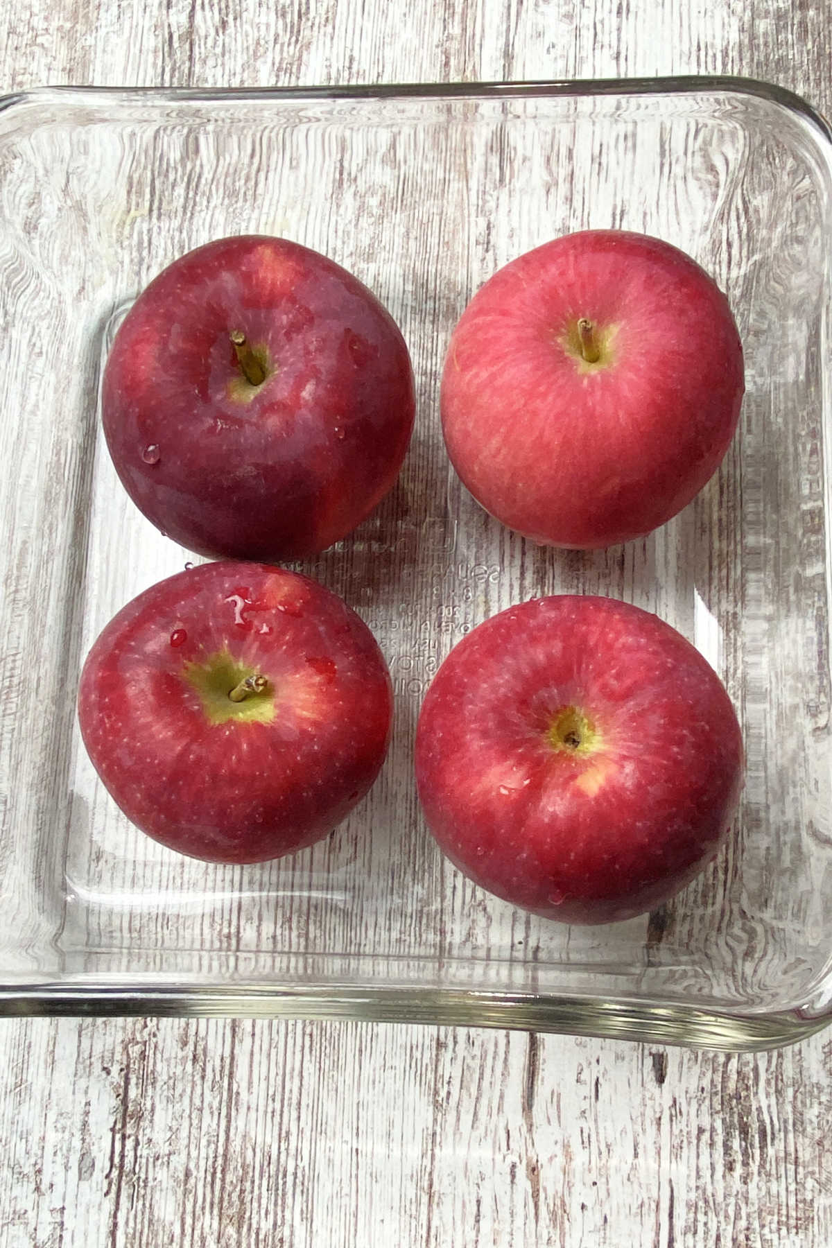 Four apples in a clear baking dish.