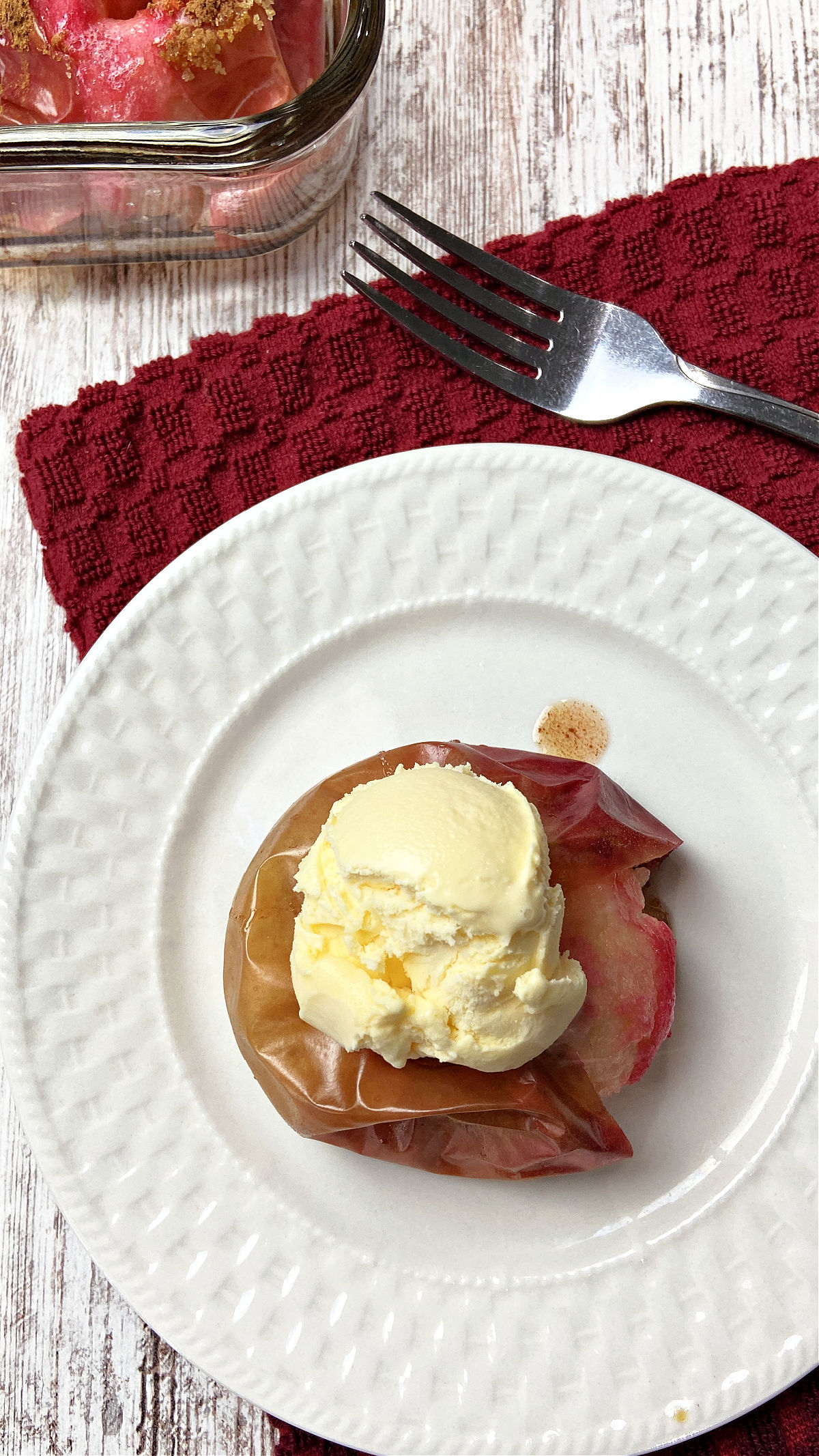 Baked apples with ice cream on top on a white plate. 