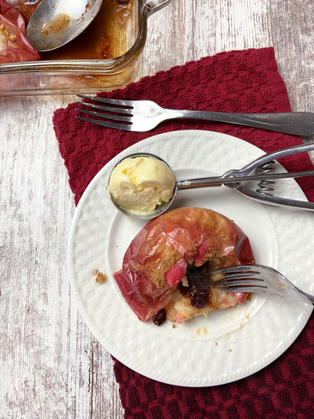 baked apple on a white plate with dried cranberries and a scoop of ice cream nearby. 