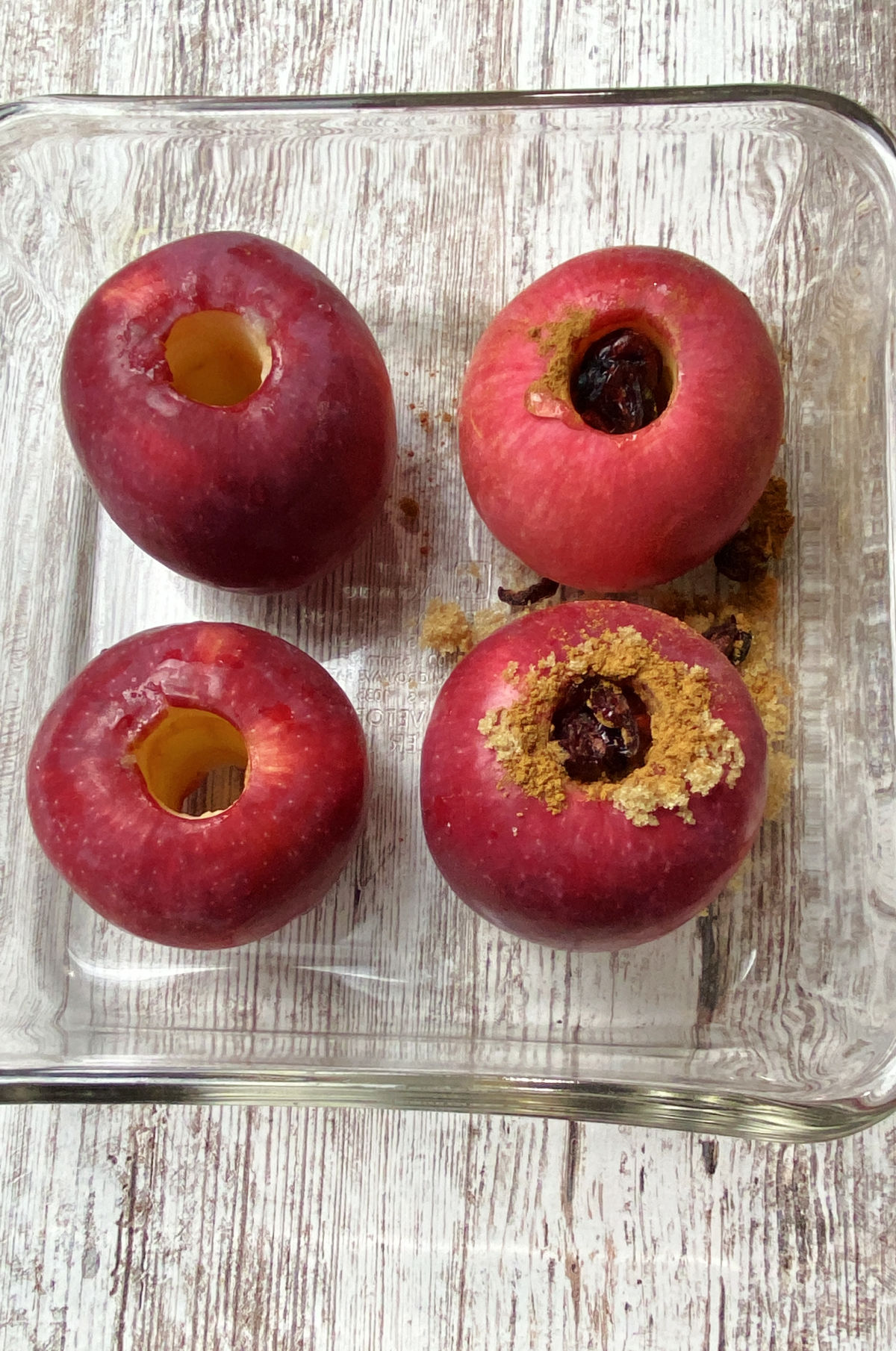 four cored apples in a clear baking dish.