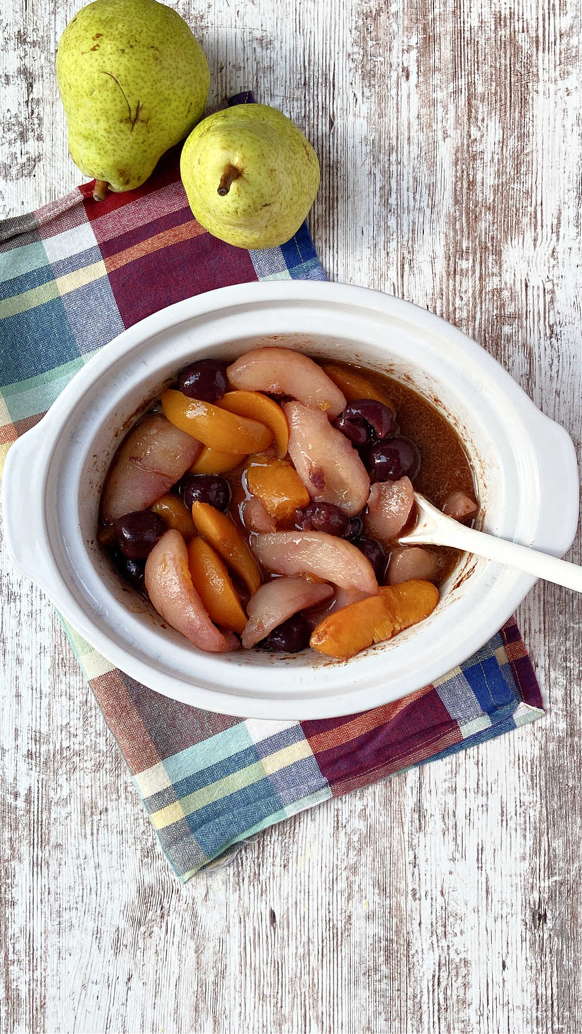 different fruit in a crock pot with a red checked towel underneath. 