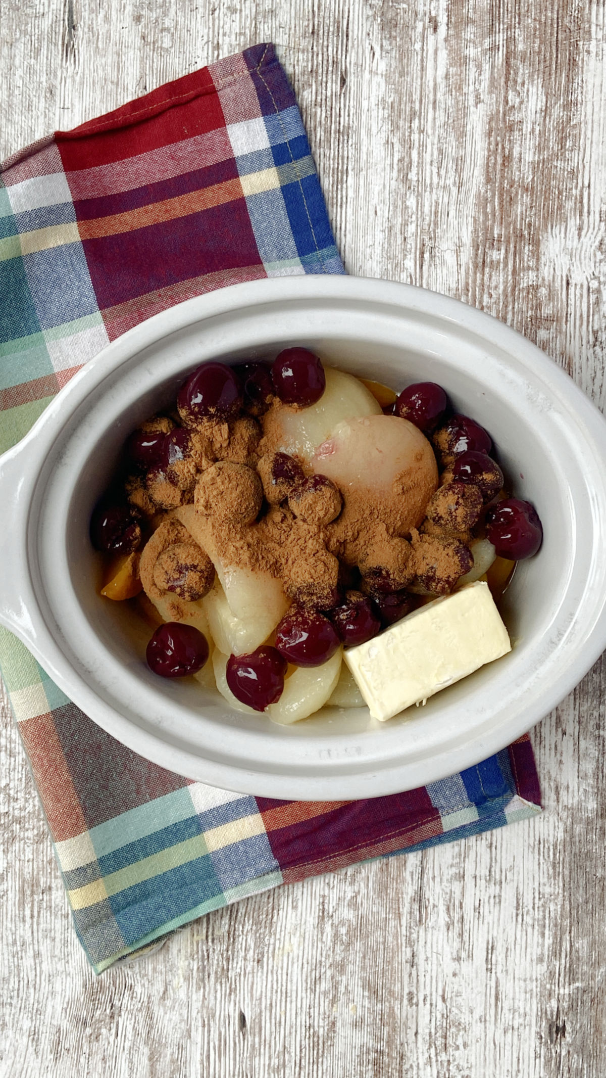 Fruit, butter and cinnamon in a crock pot with a red checked towel behind. 