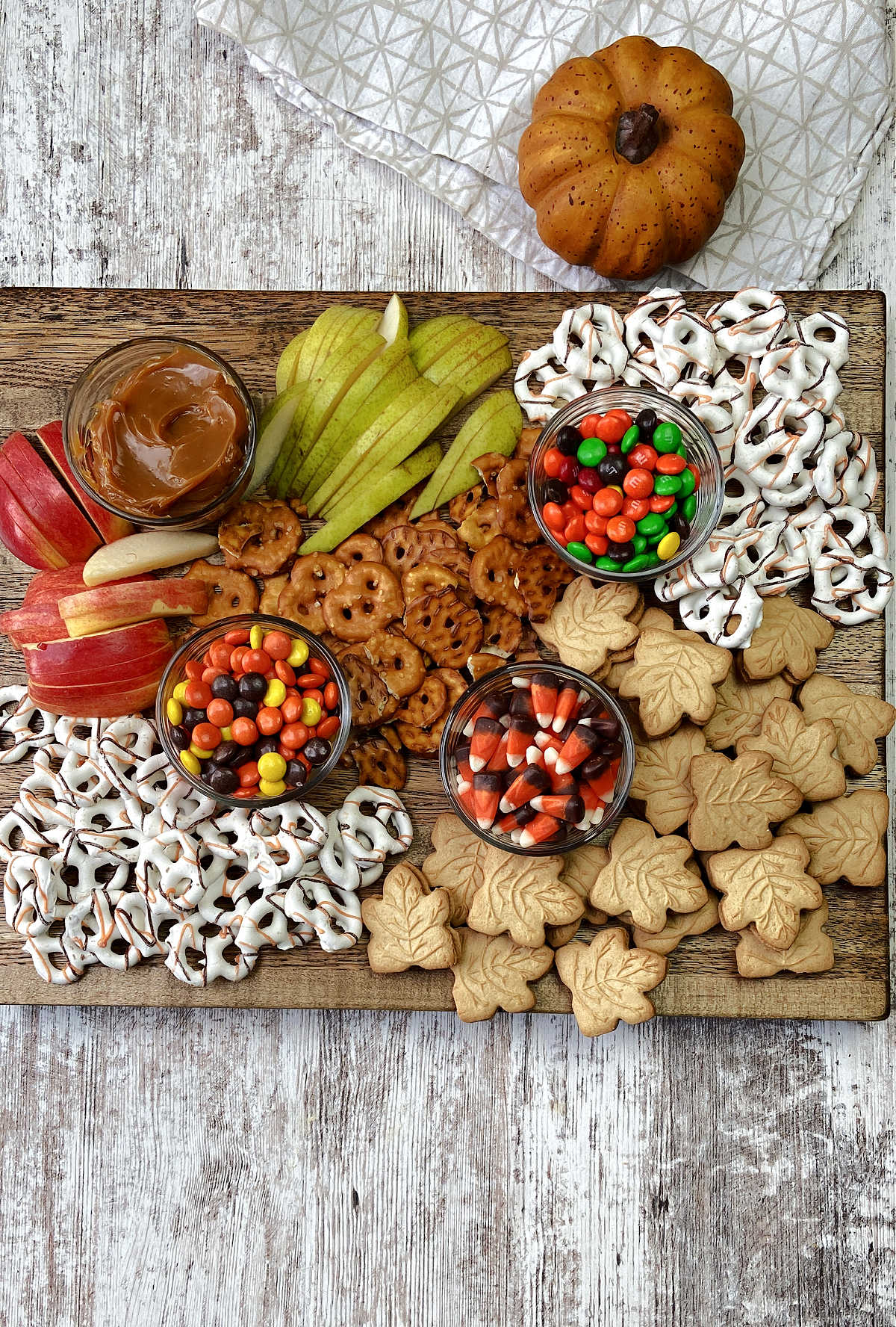 apples and pears with candy and pretzels on a board. 