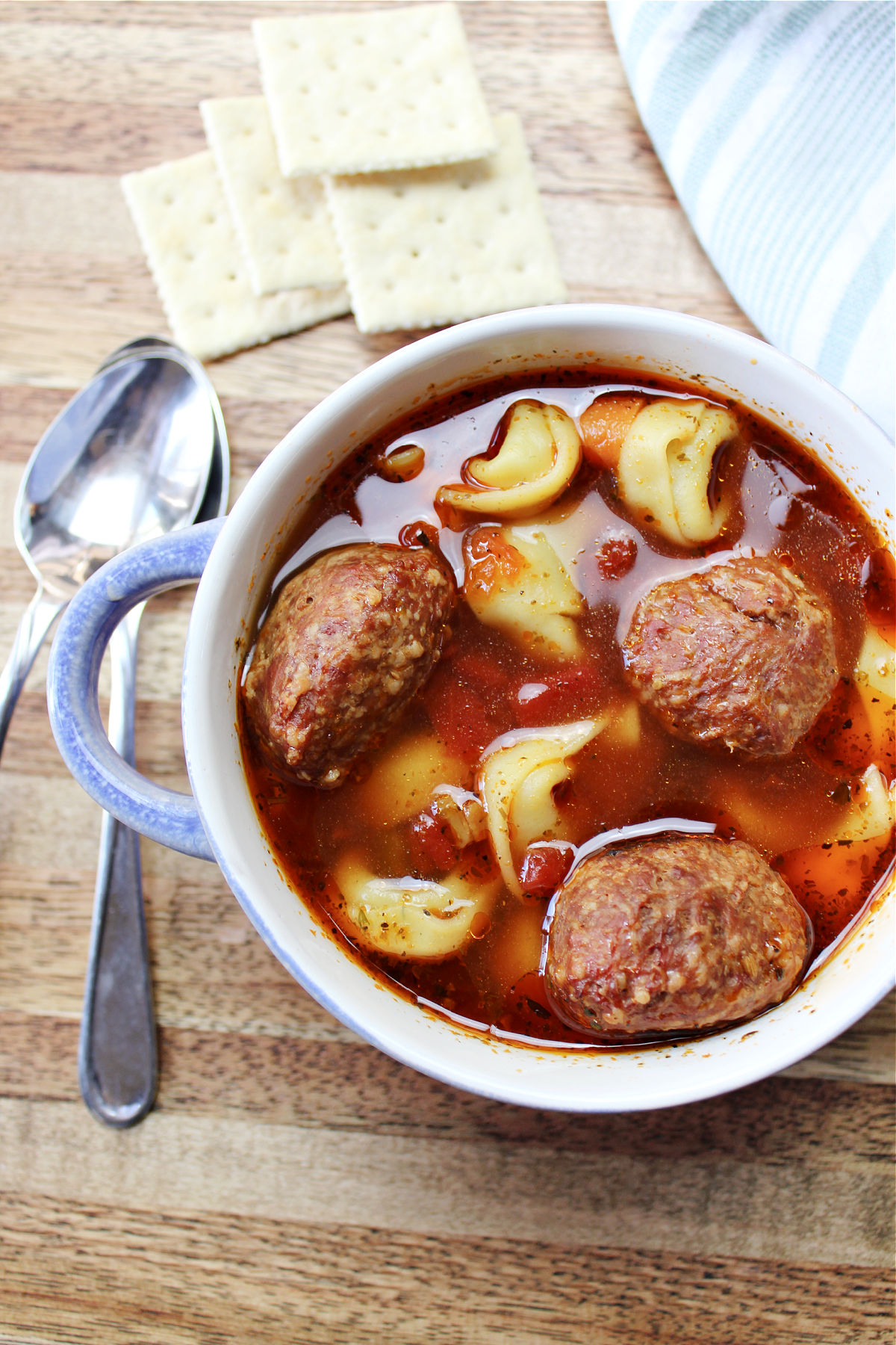 meatball soup on a brown cutting board with spoon and crackers.