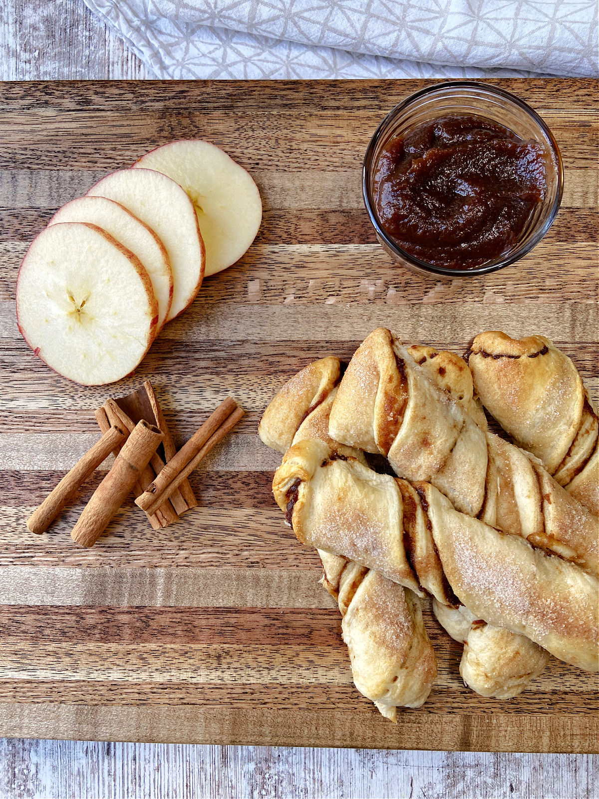 Apple pie twists on a brown cutting board with apples and apple butter. 