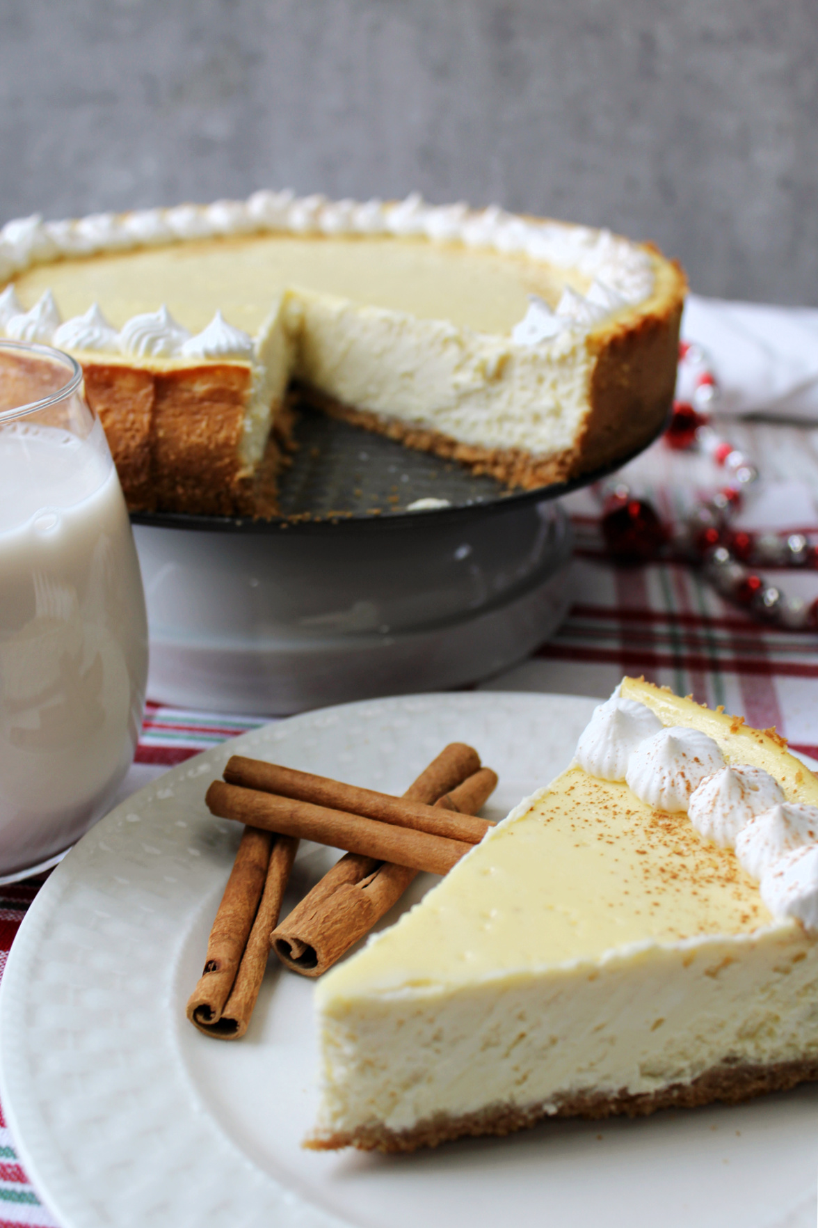 eggnog cheesecake on a white plate with cinnamon sticks. 