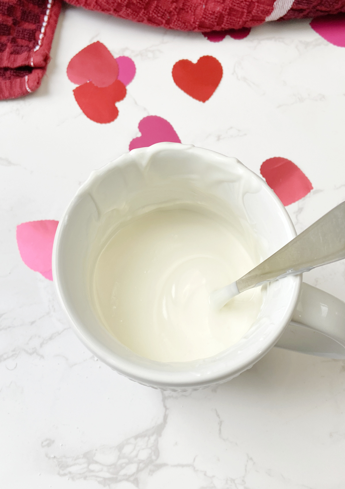 melted almond bark in a large mug with a spoon and hearts. 