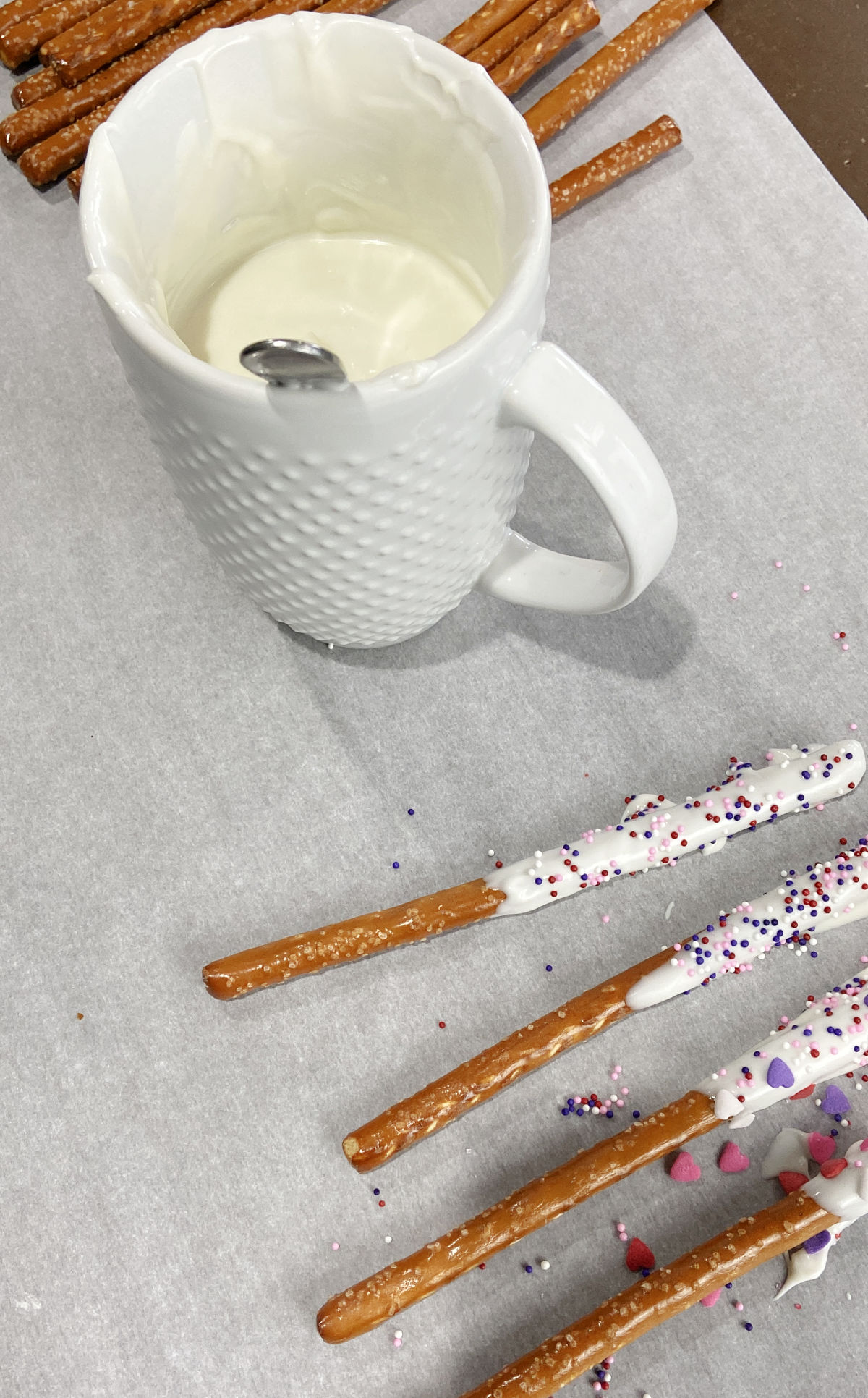 pretzel rods on parchment paper with a cup of melted almond bark. 