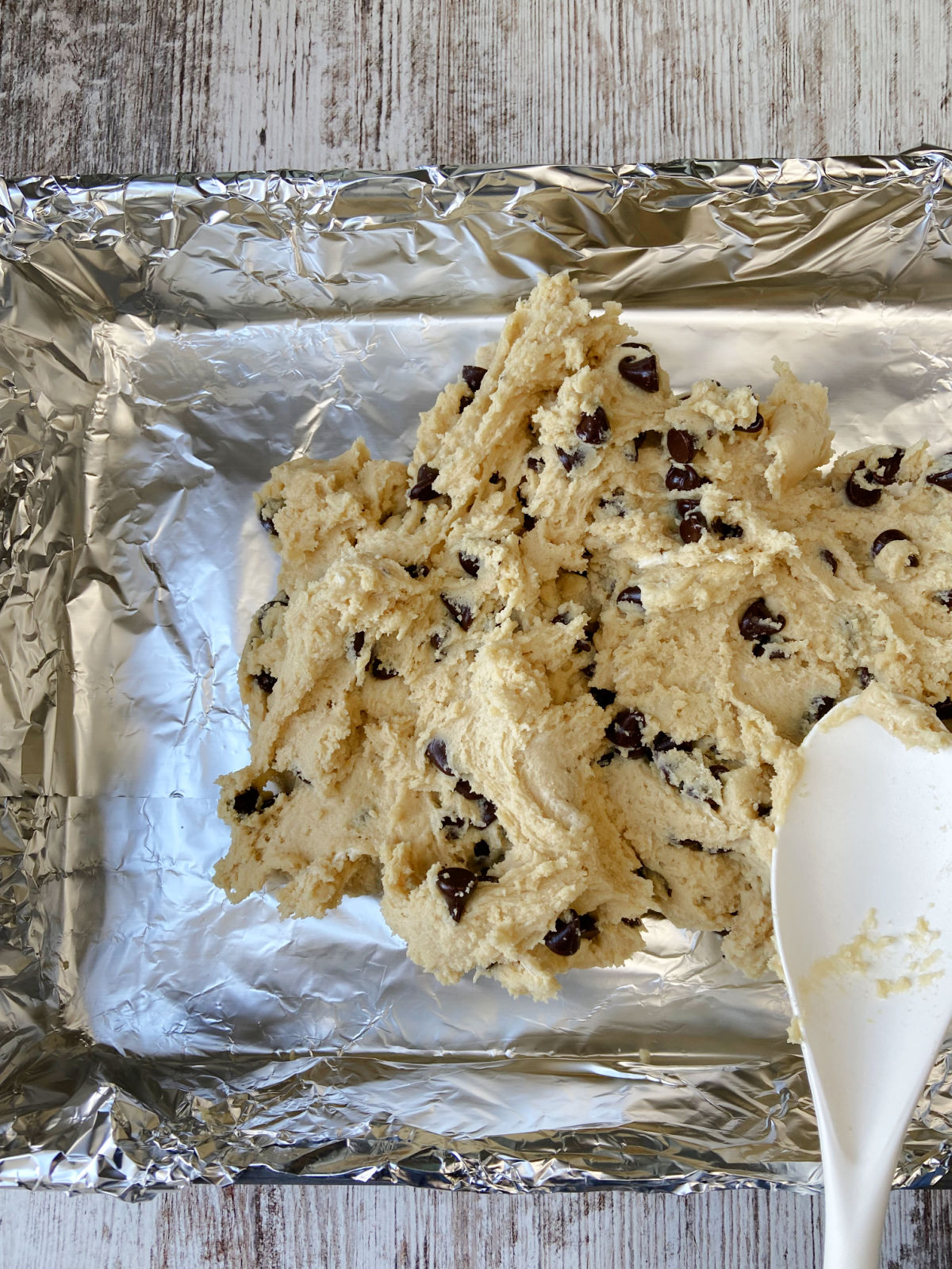 cookie dough being spread on a foil lined pan. 