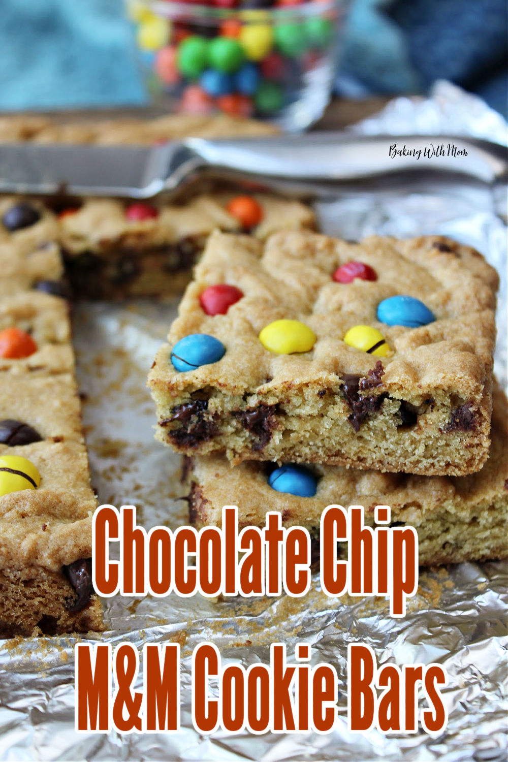 Chocolate chip M&M cookie bars on a foil sheet with a knife behind. 