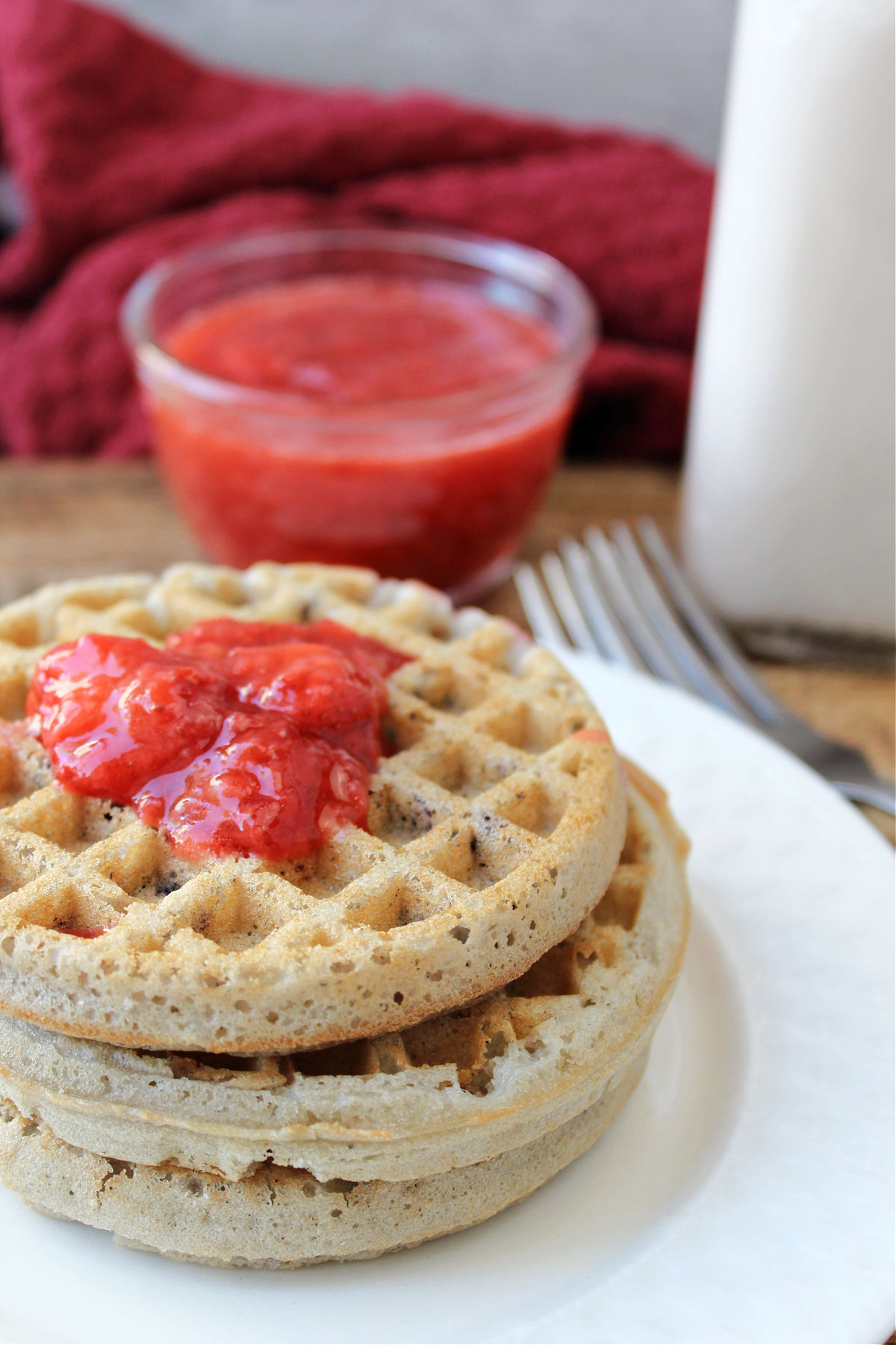 waffles on a white plate with strawberry sauce on top and in a clear bowl. 