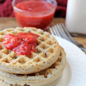 strawberry sauce on waffles sitting on a white plate with forks nearby.