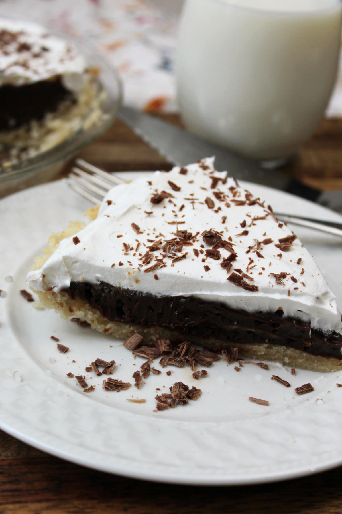 French silk pie on a white plate with a glass of milk behind. 