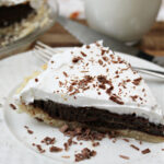 French silk pie on a white plate with a fork and milk behind.