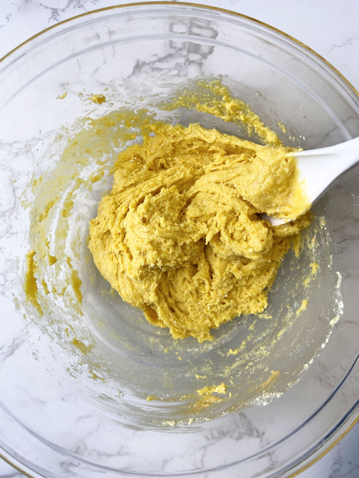 Lemon cake mixed together in a clear bowl with a white spoon. 