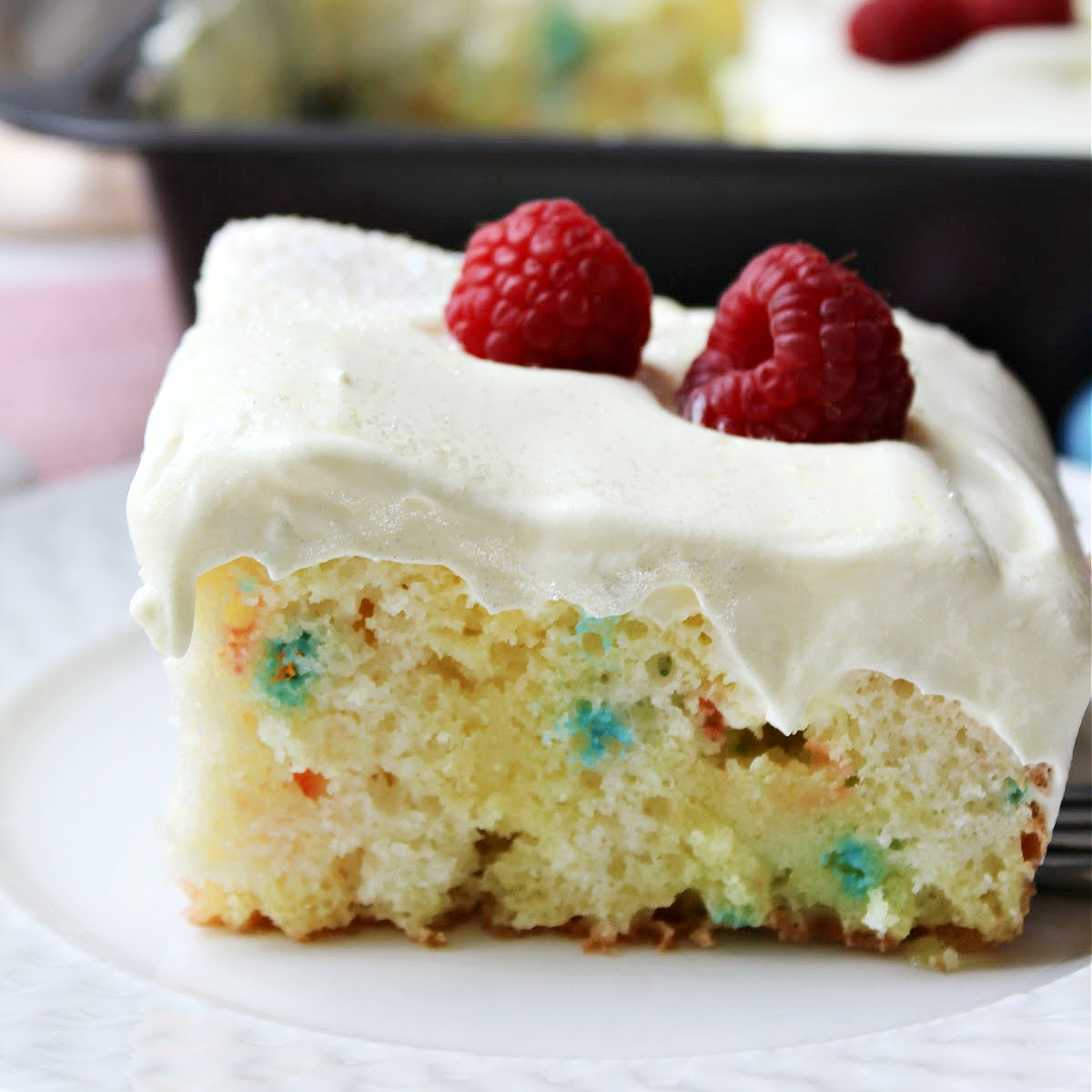 Lemon poke cake on a white plate with raspberries on top.