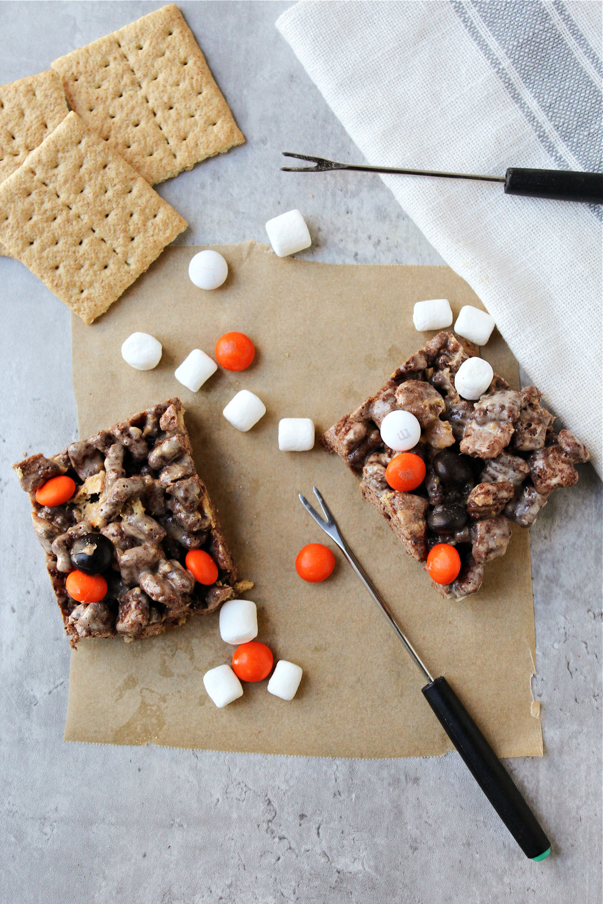 S'mores bars on brown paper with marshmallows besides. 