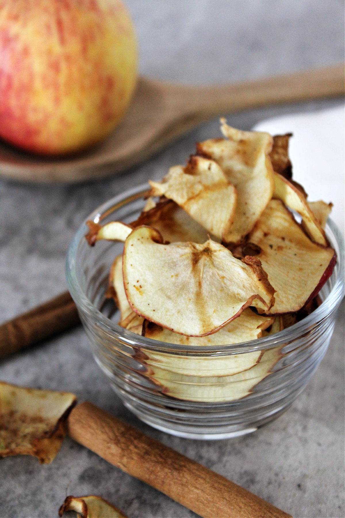 air fryer apple chips in a clear bowl with cinnamon sticks besides. 
