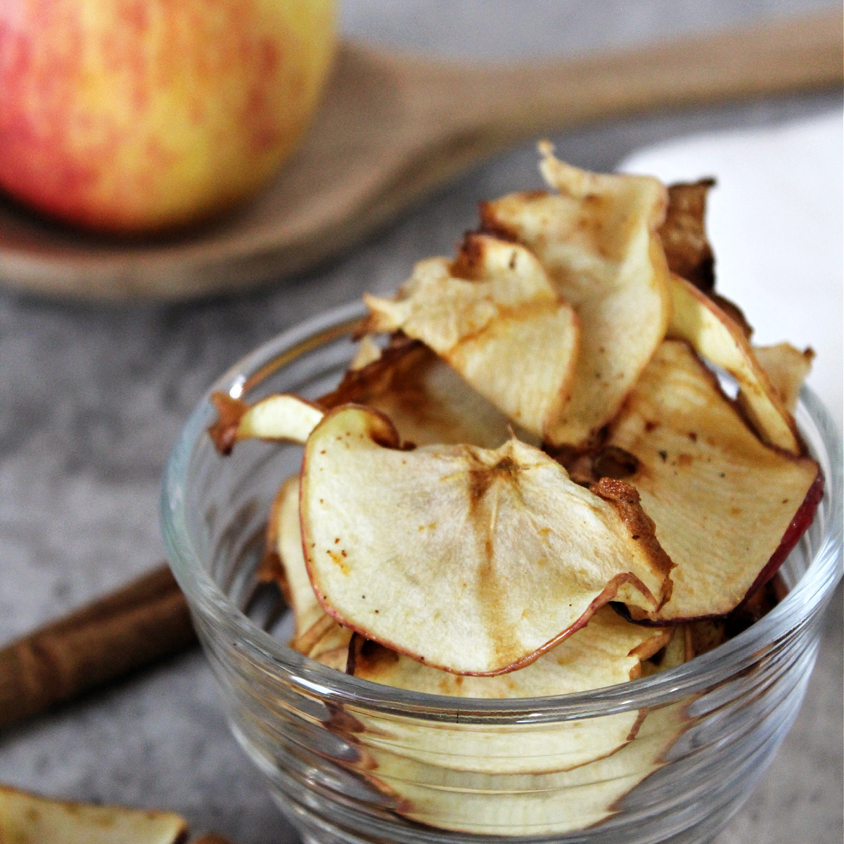 Air fryer apple chips in a clear bowl with cinnamon.