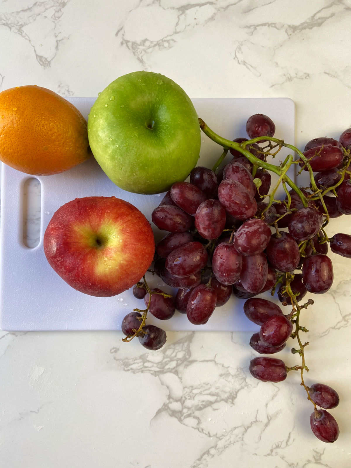 grapes, apples and oranges on a cutting board. 