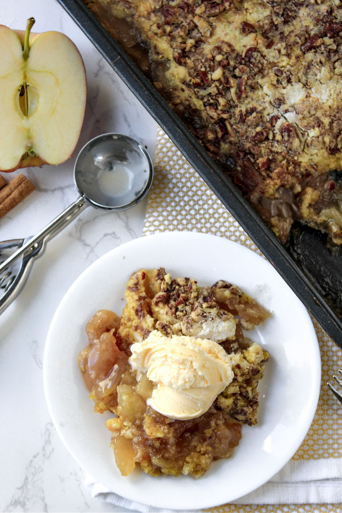 Apple dump cake with ice cream on top on a white plate. 