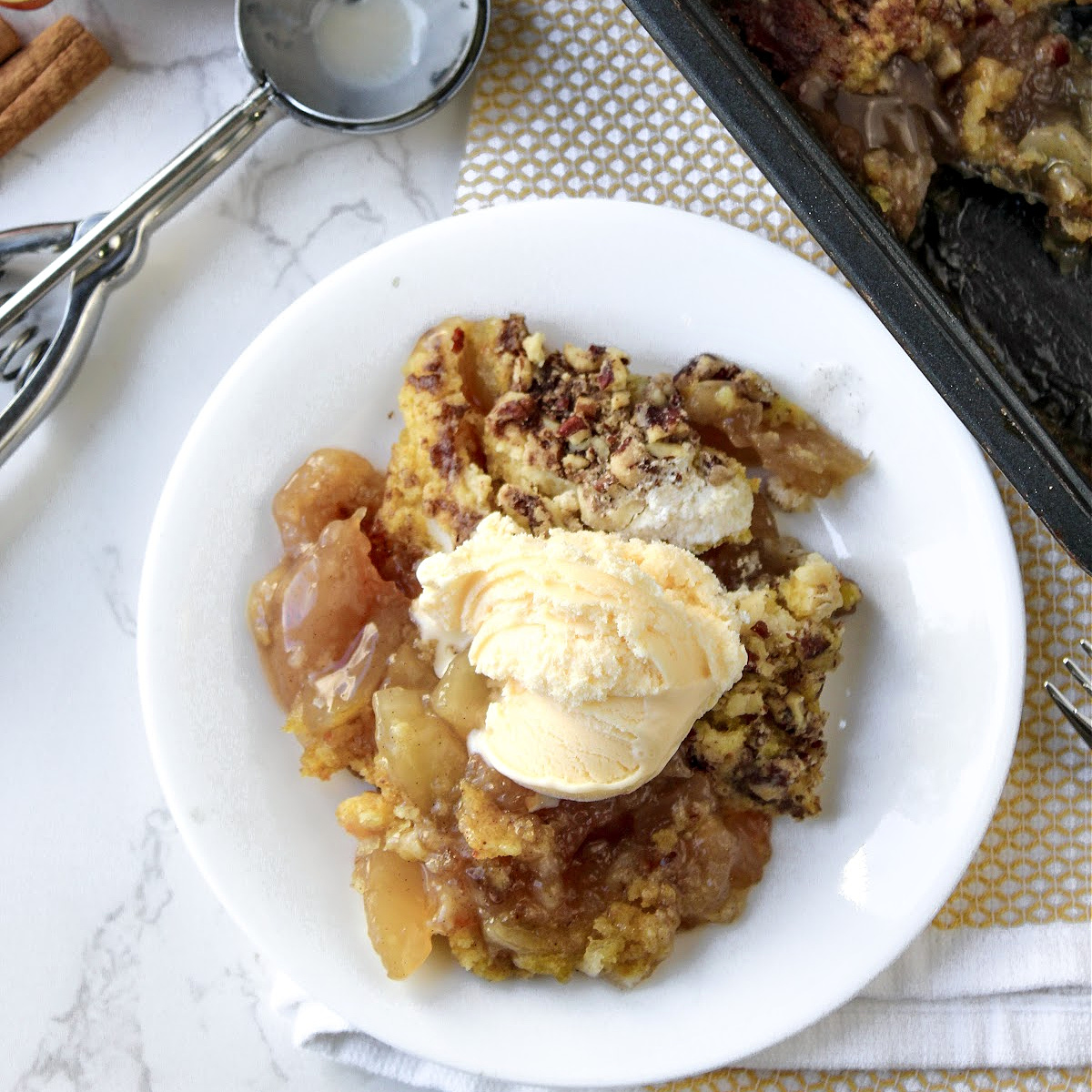 apple dump cake on a white plater with ice cream on top.