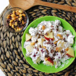 Snickers Salad with a wooden spoon and apples in a green bowl.